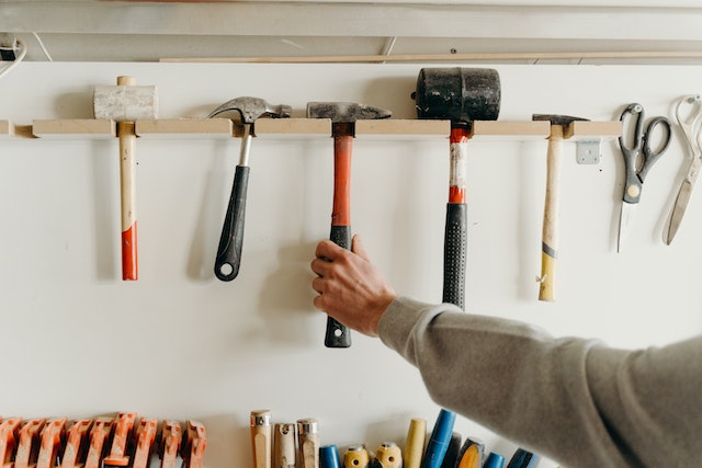 persons-hand-reaching-for-a-hammer-on-a-wall-of-tools