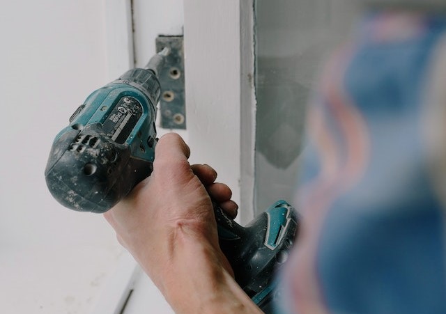 A hand holding a drill and fixing the bottom of a door.